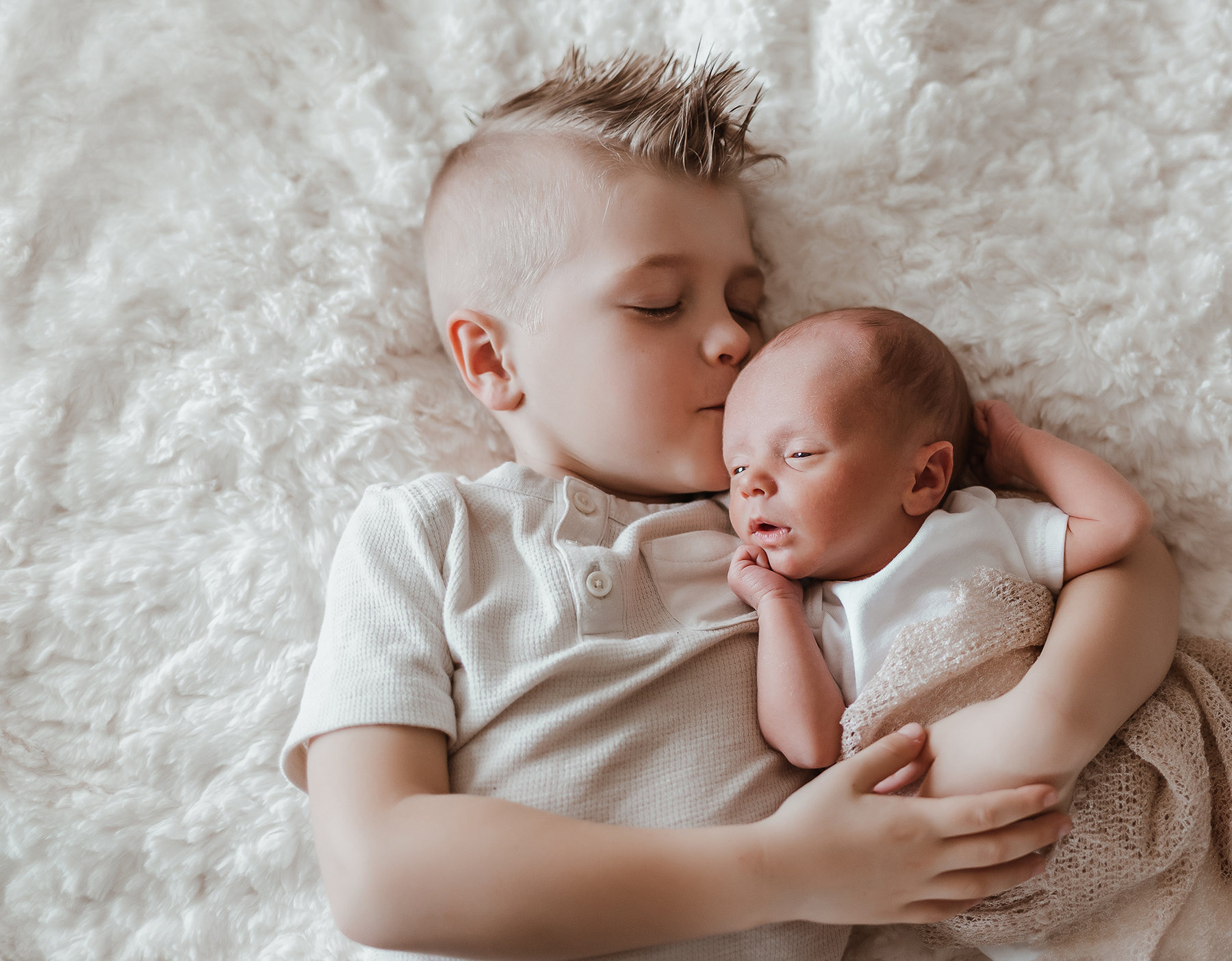 Brother snuggling with newborn baby giving him a kiss