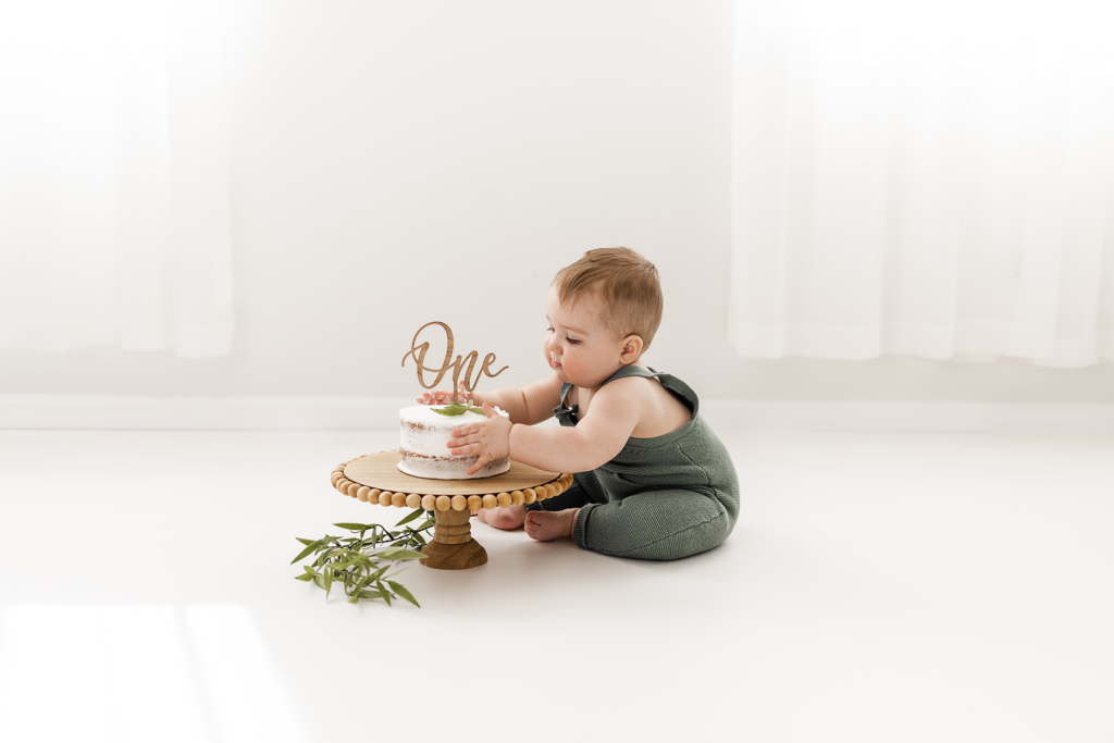 one year baby in photo studio sitting on floor with birthday cake