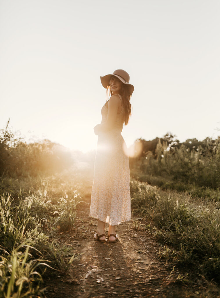 Young girl standing in field with sun setting behind her.