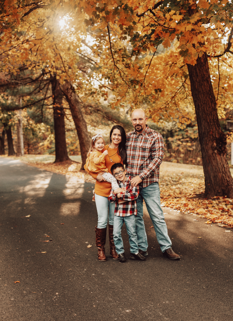 Family standing on a road surrounded by a fall scene.