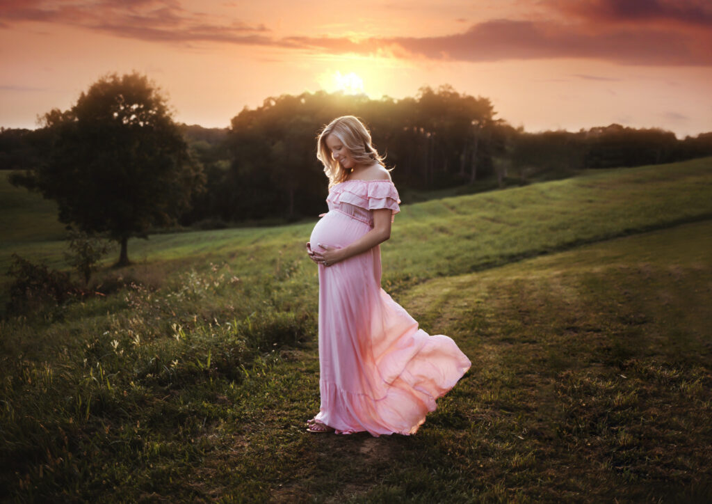 Pregnant mother holding her belly with sun setting behind her.