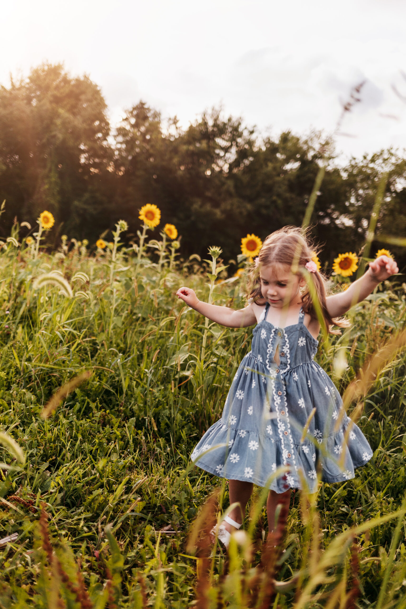 Little girl dancing in sunflower field in a blue dress